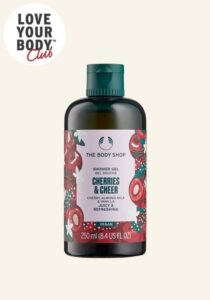 A tall cylindrical dark green plastic bottle with a dark green plastic lid and a bright pink label that has The Body Shop Cherries & Cheer Shower Gel written in dark green writing and some pictures of some bright Red Cherries on it, on a white background.