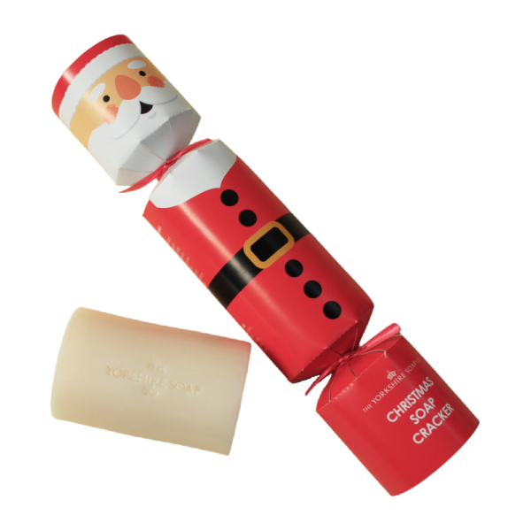 Father Christmas Has Finally Arrived In Yorkshire | The Yorkshire Soap Company Christmas 2023 Range A medium rectangular bright red and white cracker shaped block of Soap that has a Santa’s Face with a White Beard and a black belt with a bright gold buckle Engraved on it, on a white background.