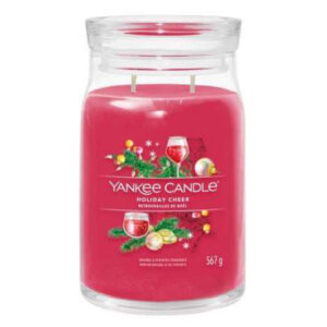 A tall cylindrical glass jar full of some bright Pink wax with a label that has Yankee Candle written in white writing, Holiday Cheer written in black writing, and a picture of a tall cylindrical wine glass full of some dark red liquid next to a bunch of some bright green grapes and some dark green holly leaves with some dark red berries on it, on a white background.