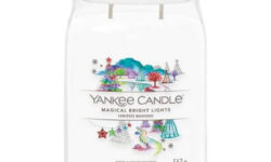 A tall cylindrical glass jar full of some creamy white wax with a label that has Yankee Candle written in white writing, Magical Bright Lights written in black writing, and a picture of a dark blue sky full of some bright white stars and clouds and a multicoloured rainbow on it, on a white background.