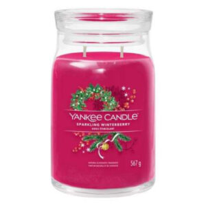 A tall cylindrical glass jar full of some bright pink wax with a label that has Yankee Candle written in white writing, Sparkling Winterberry written in black writing, and a picture of a large circular dark brown wooden christmas wreath that has some dark green holly leaves and some dark red berries coming out of the bottom of it on it, on a white background.