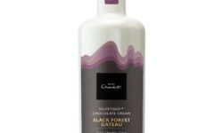 A tall cylindrical bright white glass bottle with a dark purple plastic Lid and a black label that has Hotel Chocolat Black Forest Gateaux Velvetised Cream written in bright white writing and some pictures of some dark purple waves on it, on a white background.
