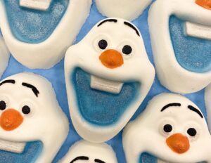 A pile of some medium bright white penguin shaped bath bombs that all have some bright orange feathers, some bright orange bellies, and some black eyes engraved on them, on a white background.