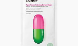 A tall rectangular bright white paper pouch that has Dr. Jart+ Cicapair™ Tiger Grass Calming Serum Mask written in bold black writing and a picture of a gradient bright pink and green capsule on it, on a white background.