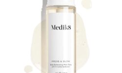 A tall cylindrical clear plastic bottle full of some clear liquid with a bright white plastic lid that has Medik8 Press & Glow™ Daily Exfoliating PHA Tonic written in bold black writing on it, on a white background.