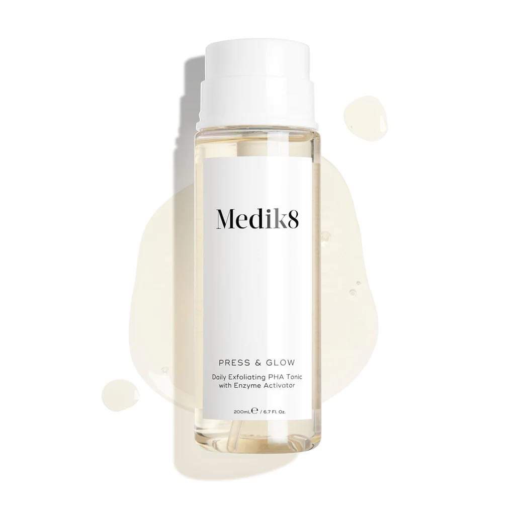 A tall cylindrical clear plastic bottle full of some clear liquid with a bright white plastic lid that has Medik8 Press & Glow™ Daily Exfoliating PHA Tonic written in bold black writing on it, on a white background.