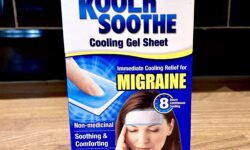 A large rectangular gradient dark blue and white cardboard box that has Kool ’n’ Soothe Migraine Cooling Strips written in bold black writing and a picture of a woman who has her eyes closed on it, on a white background.