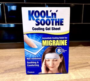A large rectangular gradient dark blue and white cardboard box that has Kool ’n’ Soothe Migraine Cooling Strips written in bold black writing and a picture of a woman who has her eyes closed on it, on a white background.