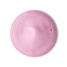A medium circular puddle of some pastel pink body scrub that has some pieces of Tagua Nut Powder and Pink Lustre running through it, on a white background.