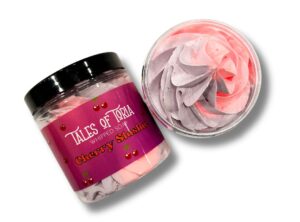 A short cylindrical clear plastic tub full of some gradient bright pink and purple whipped soap with a black plastic lid and a bright red label that has Tales of Toria written in bright white writing, Cherry Slushy Whipped Soap written in bright red writing, and some pictures of some cherries on it, on a white background.