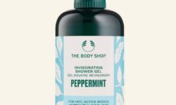 A tall cylindrical dark green plastic Bottle with a dark green plastic lid and a gradient bright blue and white label that has The Body Shop Peppermint Invigorating Shower Gel written in dark green writing and some pictures of some dark green mint leaves on it, on a white background.