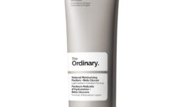 A tall flat conical bright silver plastic tube with a black plastic lid that has The Ordinary Natural Moisturising Factors + Beta Glucan written in bold black writing on it, on a white background.