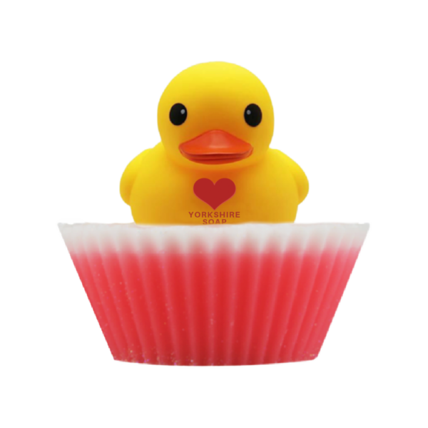 A large circular bright white cupcake shaped block of soap that has a bright Pink paper cupcake case around it and a bright Yellow Rubber Duck that has a bright Red Love Heart engraved on it’s chest on top of it, on a white background.