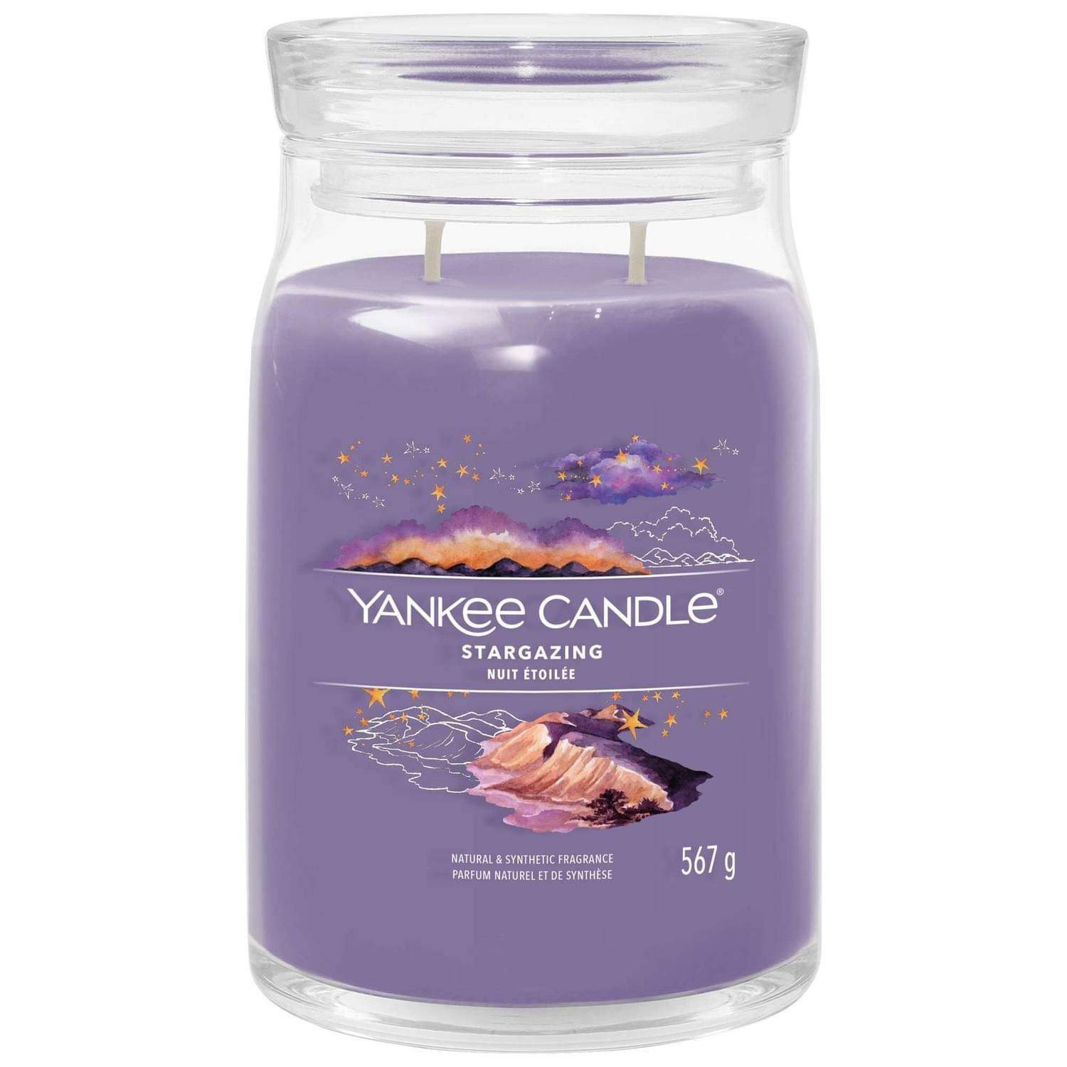 What I Thought of the Yankee Candle Advent House 2014 A tall cylindrical glass jar full of some dark purple wax with a label that has Yankee Candle written in white writing, Stargazing written in black writing, and a picture of a Mountain landscape at night with some bright white shooting stars on it, on a white background.