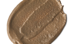 A medium circular puddle of some creamy brown face mask that has some pieces of bright white Asparagus running through it, on a white background.