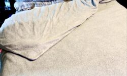 A large rectangular double Bed with a large rectangular plush dark grey headboard and some fluffy dark grey cushions that's covered in a large fluffy dark grey duvet cover, on a white background.