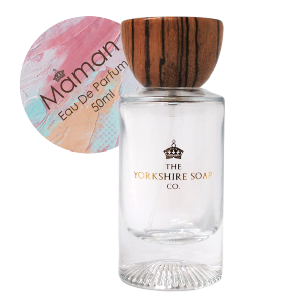 A tall rectangular clear glass bottle full of some clear liquid with a light wooden lid and a white label that has The Yorkshire Soap Company Maman Eau De Parfum written in bold black writing and a picture of a black crown on it, on a white background.