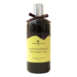 A tall and wide cylindrical plastic bottle full of some dark brown liquid with a silver plastic lid, a dark brown bow tied around it, and a gradient dark brown and bright yellow label that has The Yorkshire Soap Company Melted Chocolate Easter Egg Bath & Shower Creme written in bold black writing and a picture of a black crown on it, on a white background.
