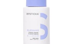 A tall conical bright white plastic tube with a dark blue plastic lid that has ZitSticka written in dark blue writing, SilkShake™ written in bold black writing, and a picture of a dark blue number five on it, on a white background.