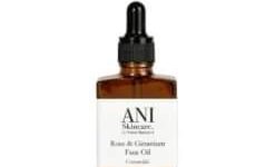 A short square amber glass bottle full of some clear liquid with a black rubber pipette lid and a white label that has Ani Skincare Rose and Geranium Face Oil written in bold black writing on it, on a white background.
