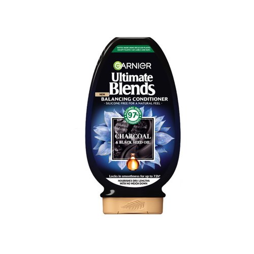 A tall rounded rectangular black plastic Bottle with a gold plastic lid and a bright green label that has Garnier Ultimate Blends Balancing Conditioner with Charcoal & Black Seed Oil written in bright white writing, a picture of a puddle of black charcoal, and a picture of some black seeds on it, on a white background.