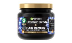A short cylindrical black plastic Tub with a black plastic lid and a bright green label that has Garnier Ultimate Blends Balancing Hair Remedy Mask with Charcoal & Black Seed Oil written in bright white writing, a picture of a puddle of black charcoal, and a picture of some black seeds on it, on a white background.