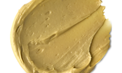 A medium circular puddle of some dark golden yellow face & Body Mask, on a white background.