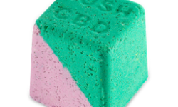 A medium gradient bright green and pink cube shaped bath bomb that has some pieces of Epsom Salt all over it and Lush CBD engraved on top of it, on a white background.