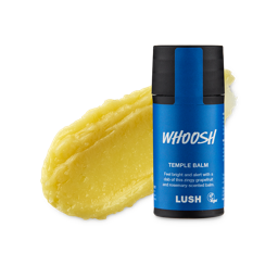 A medium circular puddle of some pale yellow temple balm next to a short cylindrical dark blue plastic tube with a black plastic lid that has Lush Whoosh Temple Balm written in bright white writing on it, on a white background.