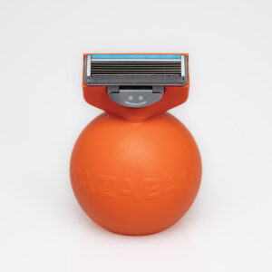 A medium spherical bright orange plastic razor that has a dark blue razor blade coming out of the top of it and Razaball engraved on it, on a white background.