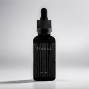 A short cylindrical brown glass bottle with a black rubber pipette lid and a black label that has runesilk elements Metal beard oil written in bold black writing and a picture of a white geometric pattern on it, on a white background.