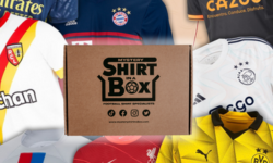 A medium rectangular cardboard box surrounded by a collection of various different coloured football shirts that all have various different coloured logos on them, on a white background.