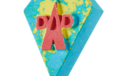 A large dark blue diamond shaped bath bomb with a bright yellow boarder that has Super Dad written in bright red writing on it, on a white background.