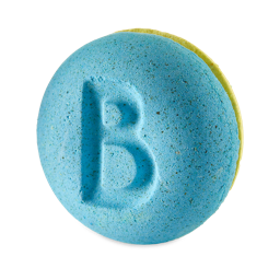 A small bright blue and yellow macaroon shaped bath bomb that has some bright white buttercream in the middle of it and a letter B engraved on it, on a white background.