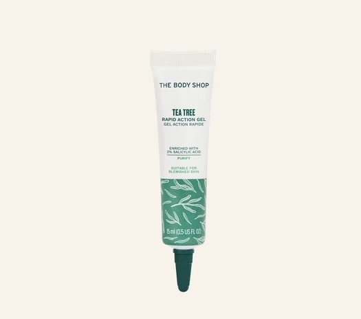 Quick!! I Need To Get Rid Of This Spot! | The Body Shop Tea Tree Rapid Action Gel A long and thin bright white plastic tube that has The Body Shop Tea Tree Rapid Action Gel written in bold black writing, a picture of a dark green stripe, and a picture of some dark green Tea Tree Leaves on it, on a white background.