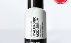 A short cylindrical white plastic bottle with a black plastic lid and a black label that has The INKEY List Hyaluronic Acid Serum written in bold black writing on it., on a white background.