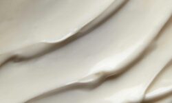 A medium circular puddle of some glossy creamy beige Moisturiser, on a white background.