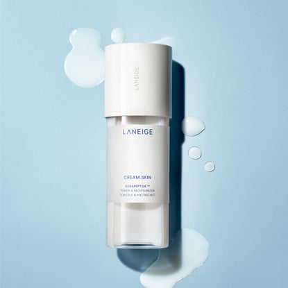 The Prestige Of Japanese Skincare | Laneige Cream Skin Toner & Moisturiser A tall cylindrical bright white plastic bottle with a bright white plastic lid that has Laneige Cream Skin Toner & Moisturiser written in dark bluie writing on it, on a white background.
