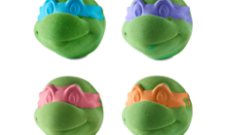 A large bright green turtle’s head shaped bath bomb that has a dark red Bandana engraved on it next to a large bright green turtle’s head shaped bath bomb that has a bright orange Bandana engraved on it, a large bright green turtle’s head shaped bath bomb that has a dark blue Bandana engraved on it, and a large bright green turtle’s head shaped bath bomb that has a bright purple Bandana engraved on it, on a white background.