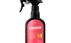 A tall black plastic kitchen spray bottle with a bright fuchsia pink label that has Lush Passion Body Spray written in bright white writing on it, on a white background.