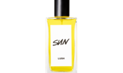 A tall rectangular clear glass bottle full of some bright Canary Yellow liquid with a bright white label that has Lush Sun Eau De Cologne written in bold black writing on it, on a white background.