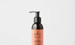 A short cylindrical dark brown plastic bottle with a black plastic pump lid and a peachy pink label that has Sukin Radiance Gel Cleanser written in bold black writing on it, on a white background.