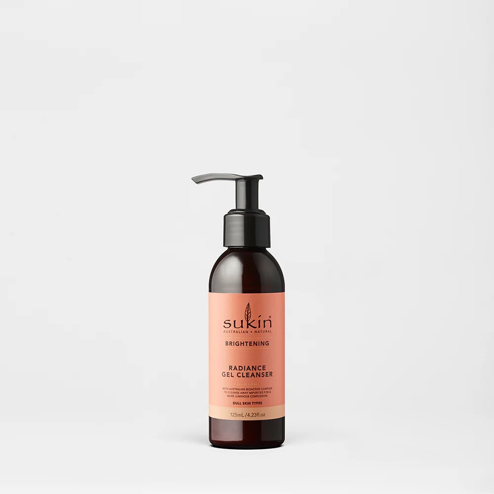 I Love Having Cleansed & Radiant-Looking Skin | Sukin Radiance Gel Cleanser A short cylindrical dark brown plastic bottle with a black plastic pump lid and a peachy pink label that has Sukin Radiance Gel Cleanser written in bold black writing on it, on a white background.