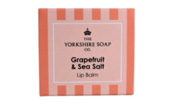 A short square bright peach cardboard box that has The Yorkshire Soap Company Grapefruit & Sea Salt Lip Balm written in bold black writing and a picture of a black crown on it, on a white background.
