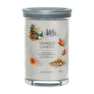 A tall cylindrical glass jar full of some creamy white wax with a label that has Yankee Candle written in bright white writing, Woodland Weekend Memories written in bright white writing, and a picture of a large dark wooden log cabin surrounded by some large dark green pine trees and a campfire on it, on a white background.