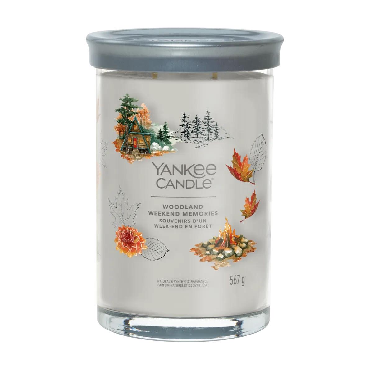 #BlindGuyAdventures | Christmas Weekend Madness A tall cylindrical glass jar full of some creamy white wax with a label that has Yankee Candle written in bright white writing, Woodland Weekend Memories written in bright white writing, and a picture of a large dark wooden log cabin surrounded by some large dark green pine trees and a campfire on it, on a white background.
