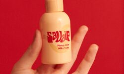 A short cylindrical light peach plastic bottle with a light peach plastic pump lid and a gradient bright orange and red label that has Savaip Plump Glow Milky Toner written in bright red writing on it, on a white background.