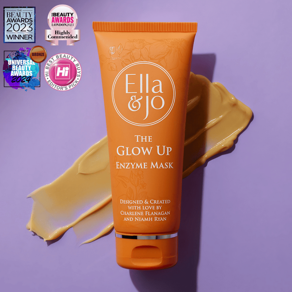 It's Time To Give My Face A Proper Glow Up | Ella And Jo The Glow Up Enzyme Mask A tall conical bright orange plastic tune with a bright orange plastic lid that has Ella and Jo The Glow Up Enzyme Mask written in bright white writing and some pictures of some pale orange flowers and leaves on it, on a pale lilac background.