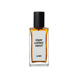 A short rectangular glass perfume bottle full of some translucent amber liquid with a metallic black lid and a white label that has Lush Vegan Leather Jacket perfume written in bold black writing on it, on a white background.