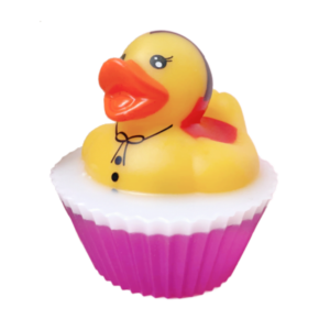 A short cylindrical bright white cupcake shaped block of soap on a bright white cupcake liner that has a bright yellow rubber duck with a bright orange beak, some black eyes, a black bow tie and some black buttons sat on top of it, on a white background.